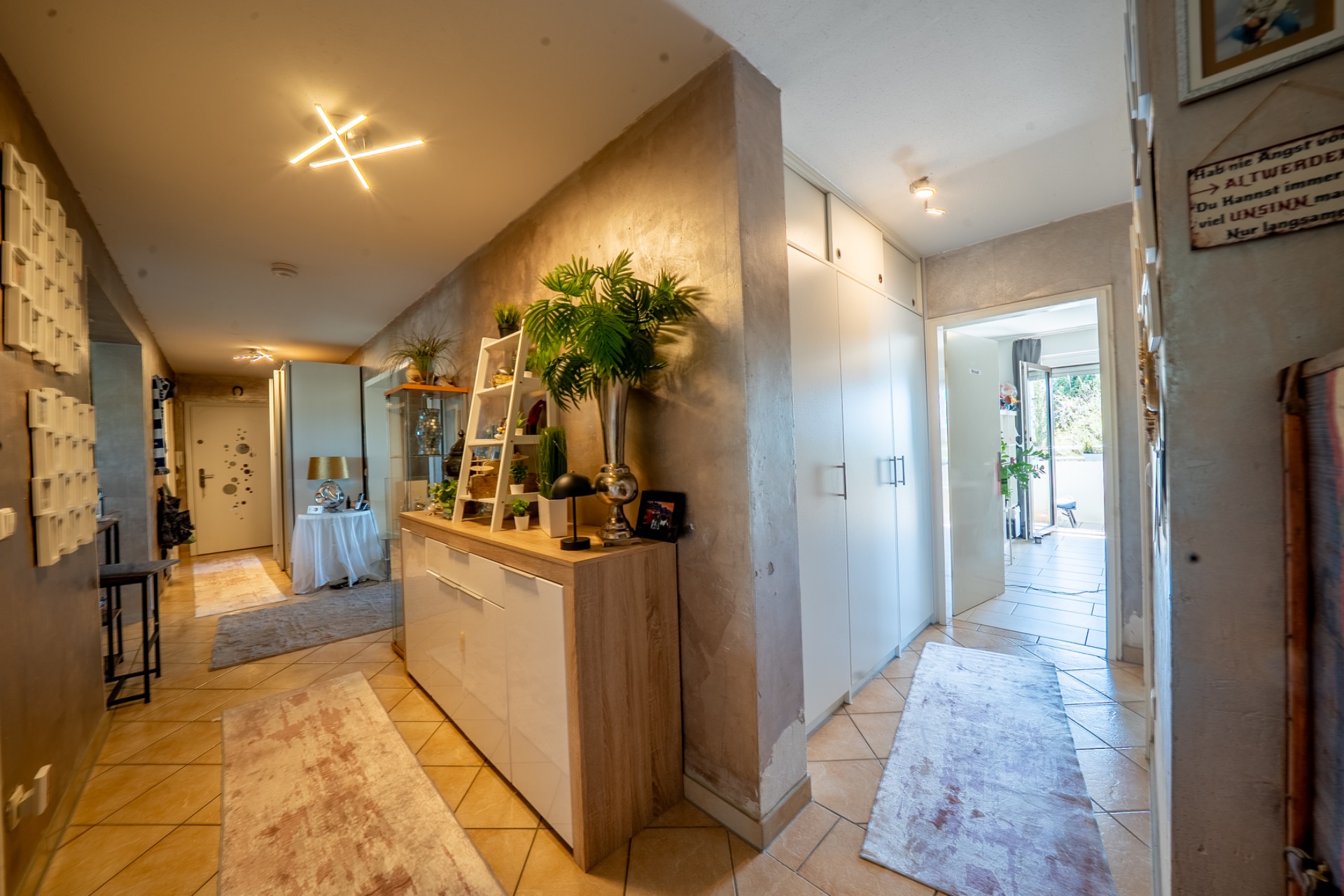 Heller Flur mit Kommode, Pflanzen, Teppichen und Zugang zu weiteren Zimmern in einer Wohnung.