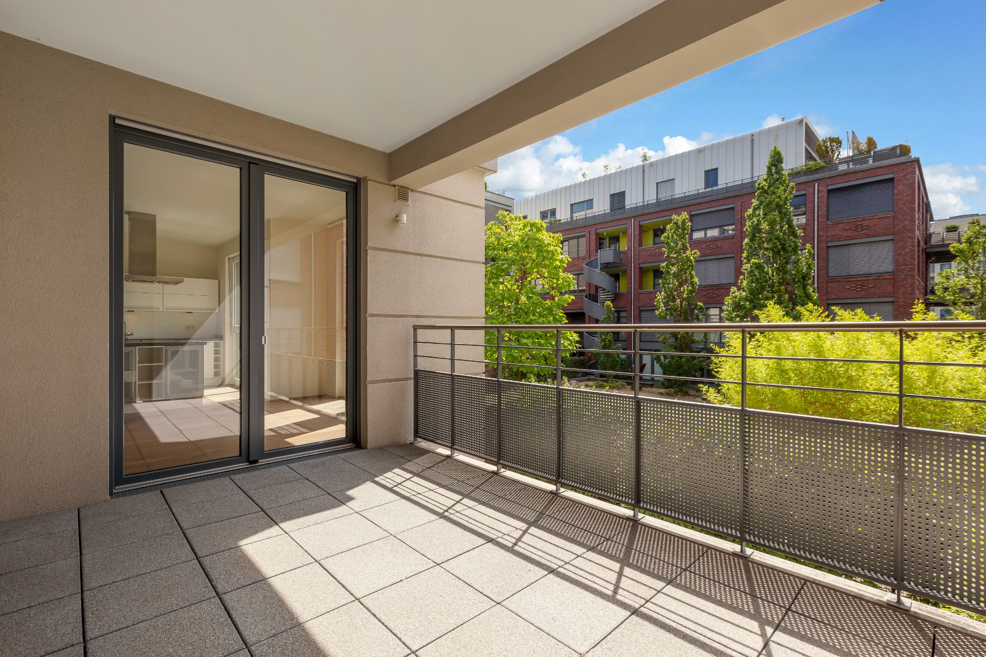 Großer Balkon mit Fliesenboden und Blick auf moderne Wohngebäude und Bäume.