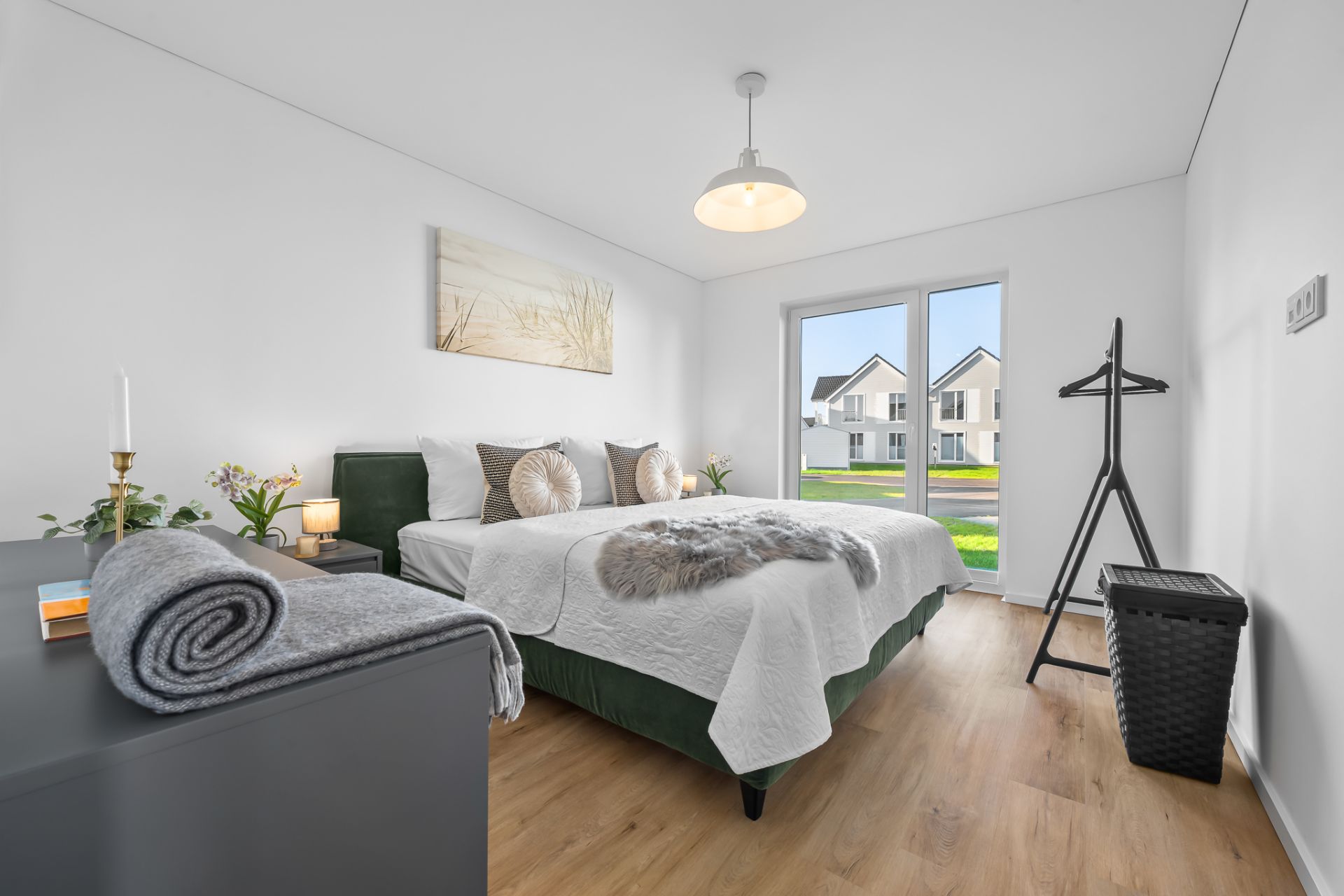 Modernes Schlafzimmer mit Doppelbett, Kommode, Fenster und Blick auf Häuser im Freien.