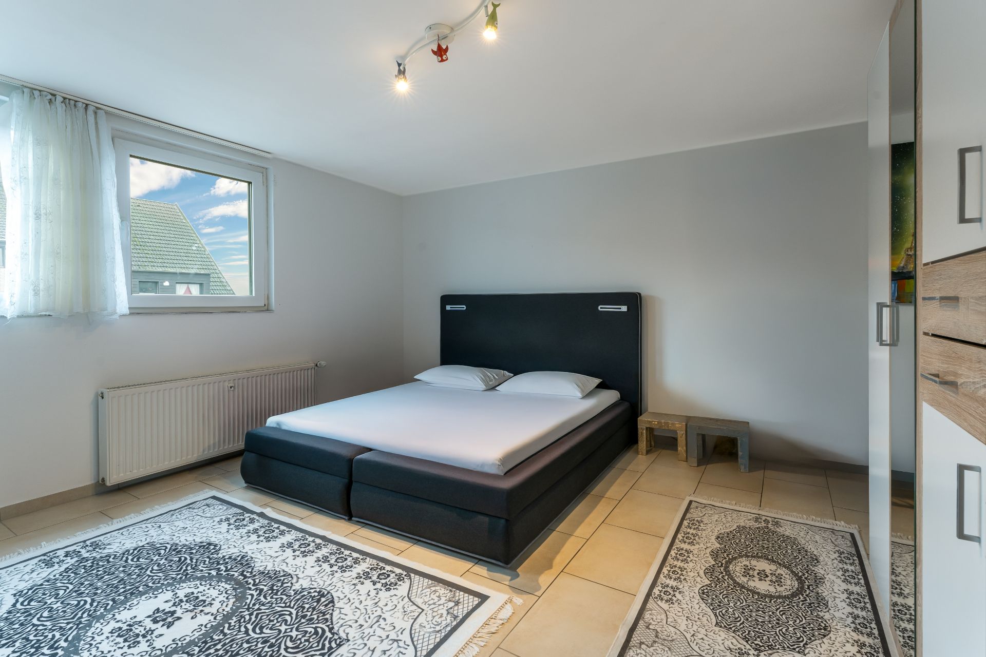Helles Schlafzimmer mit Doppelbett, zwei Teppichen, Fenster und Kleiderschrank.