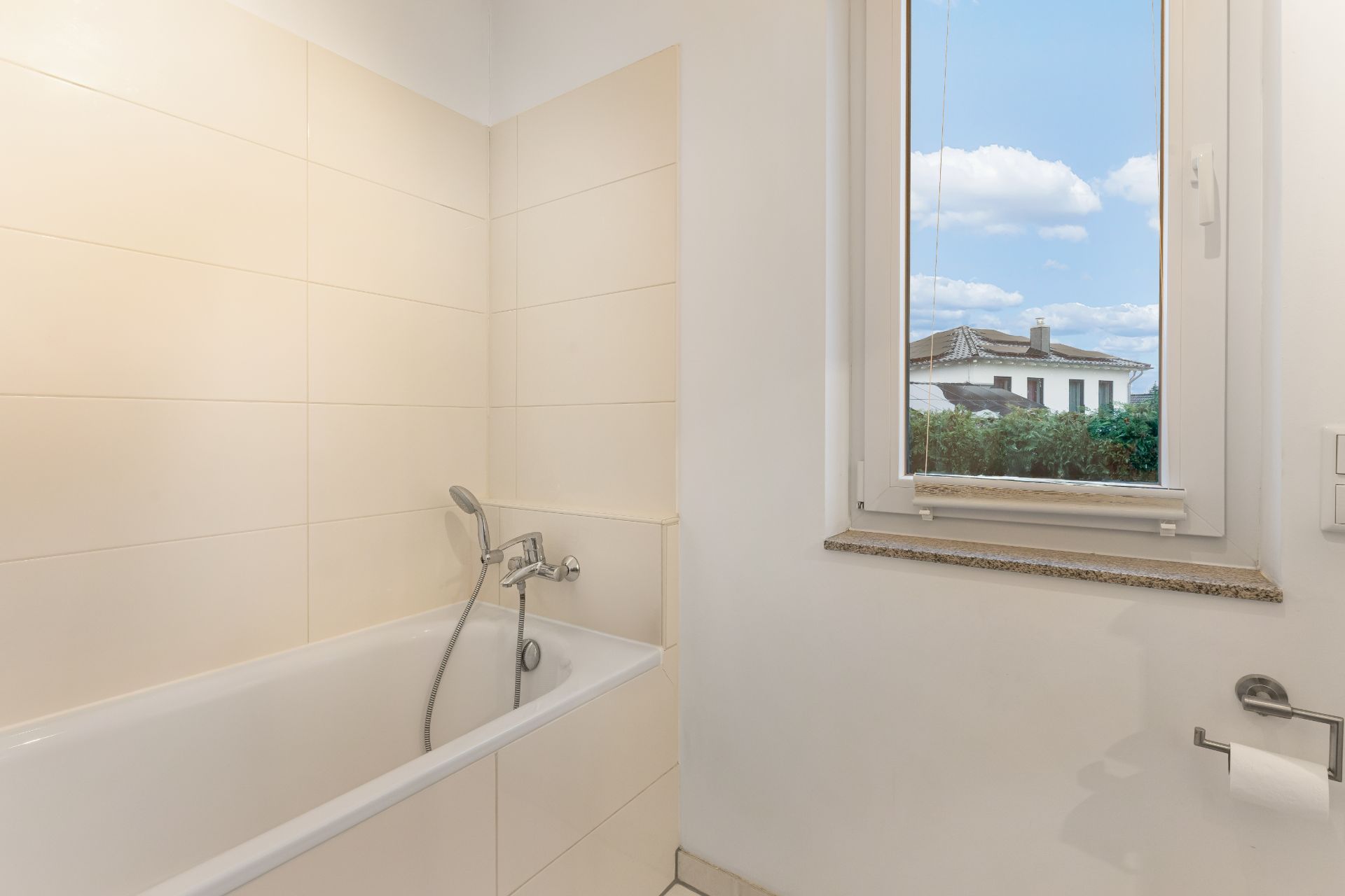 Badewanne mit Handbrause neben Fenster mit Ausblick, daneben Toilettenpapierhalter.