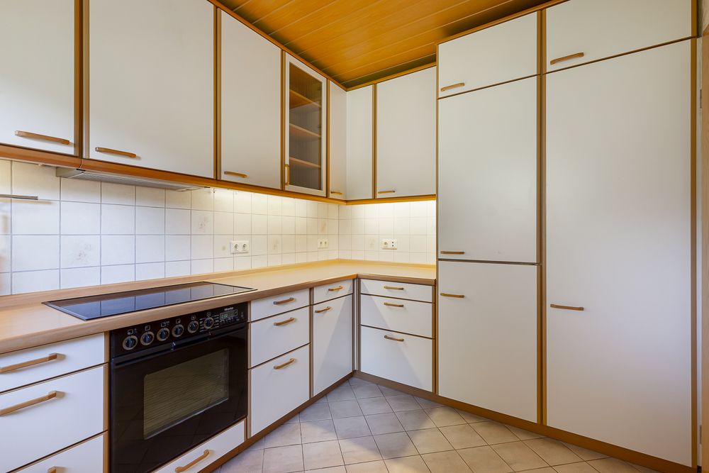 Moderne Einbauküche mit weißen Schränken, Elektroherd und Holzdetails.