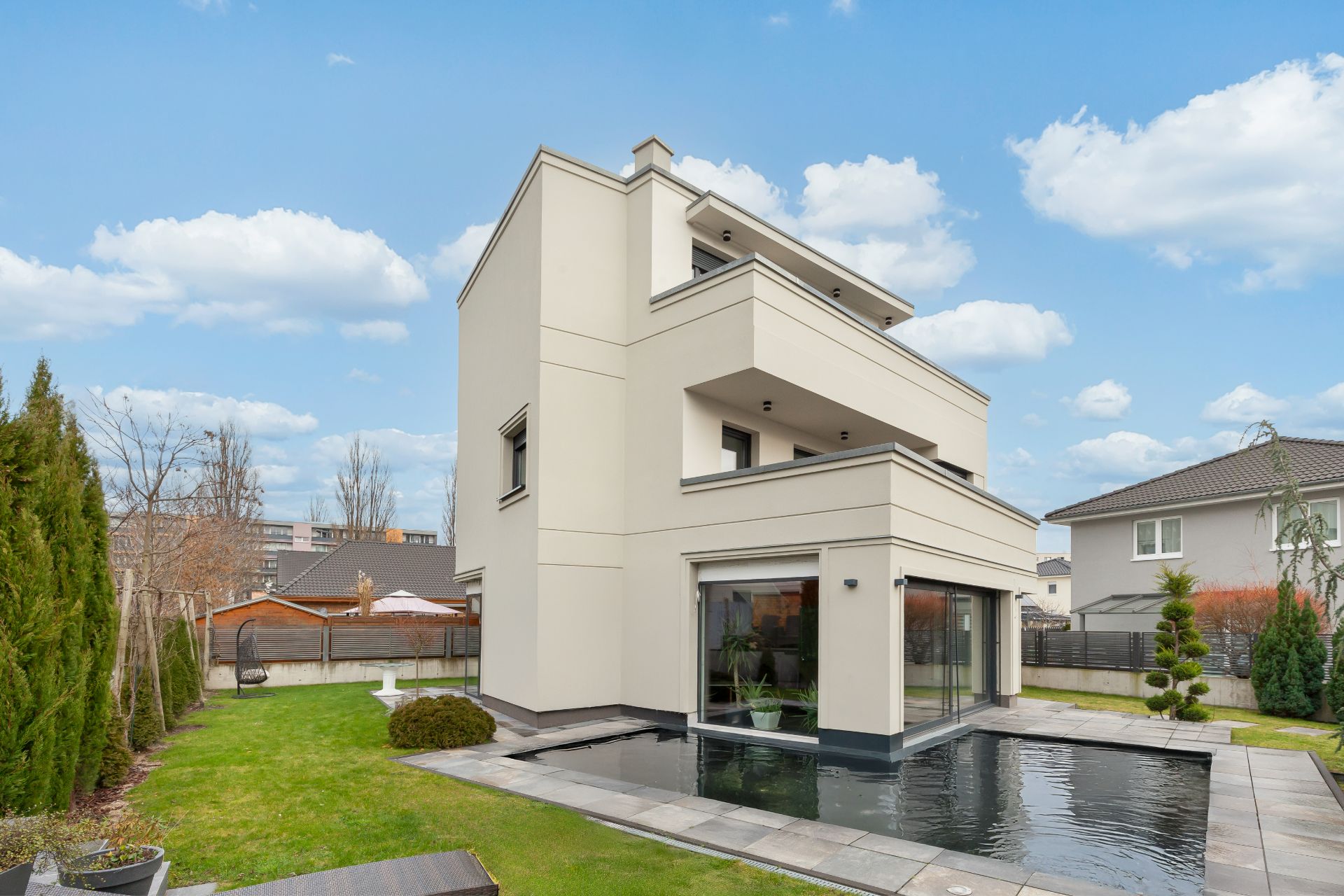 Modernes, dreistöckiges Wohnhaus mit Terrasse, großem Fenster und Wasserbecken im Garten.