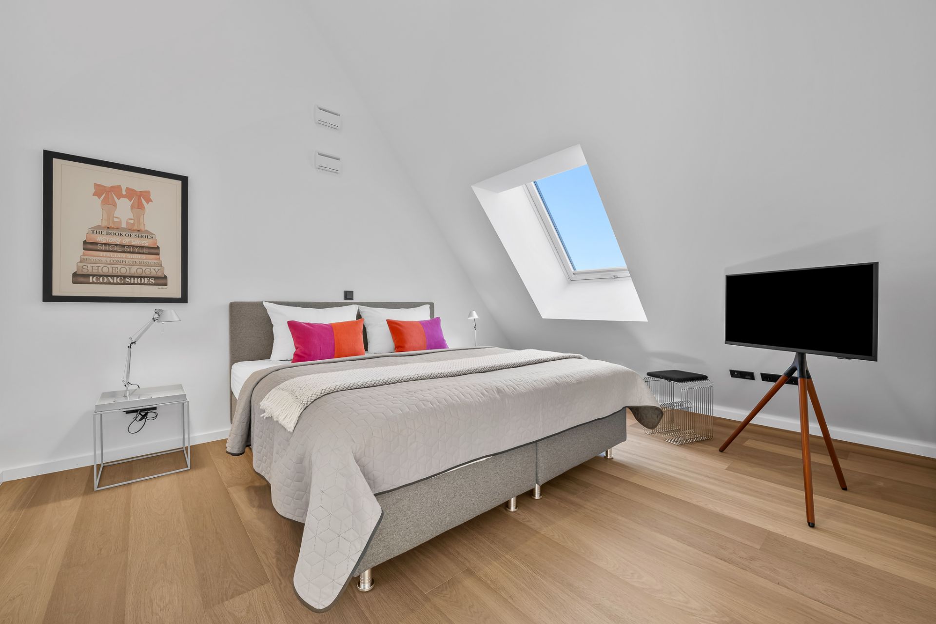 Modernes Schlafzimmer mit Doppelbett, bunten Kissen, Bild an der Wand und Dachfenster.
