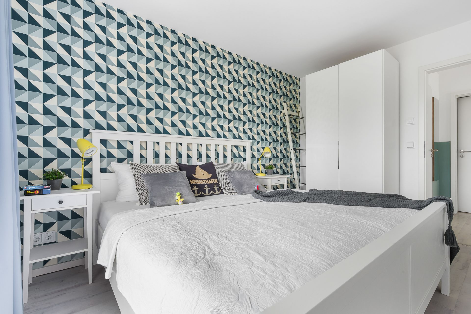 Modernes Schlafzimmer mit gemusterter Wand, weißem Bett und Kleiderschrank.