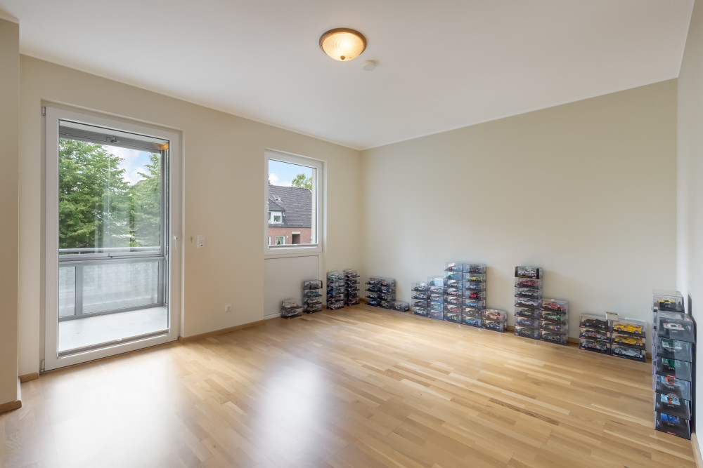 Helles Zimmer mit Holzboden, viele Modellautos in Vitrinen an den Wänden, Fenster und Balkontür.