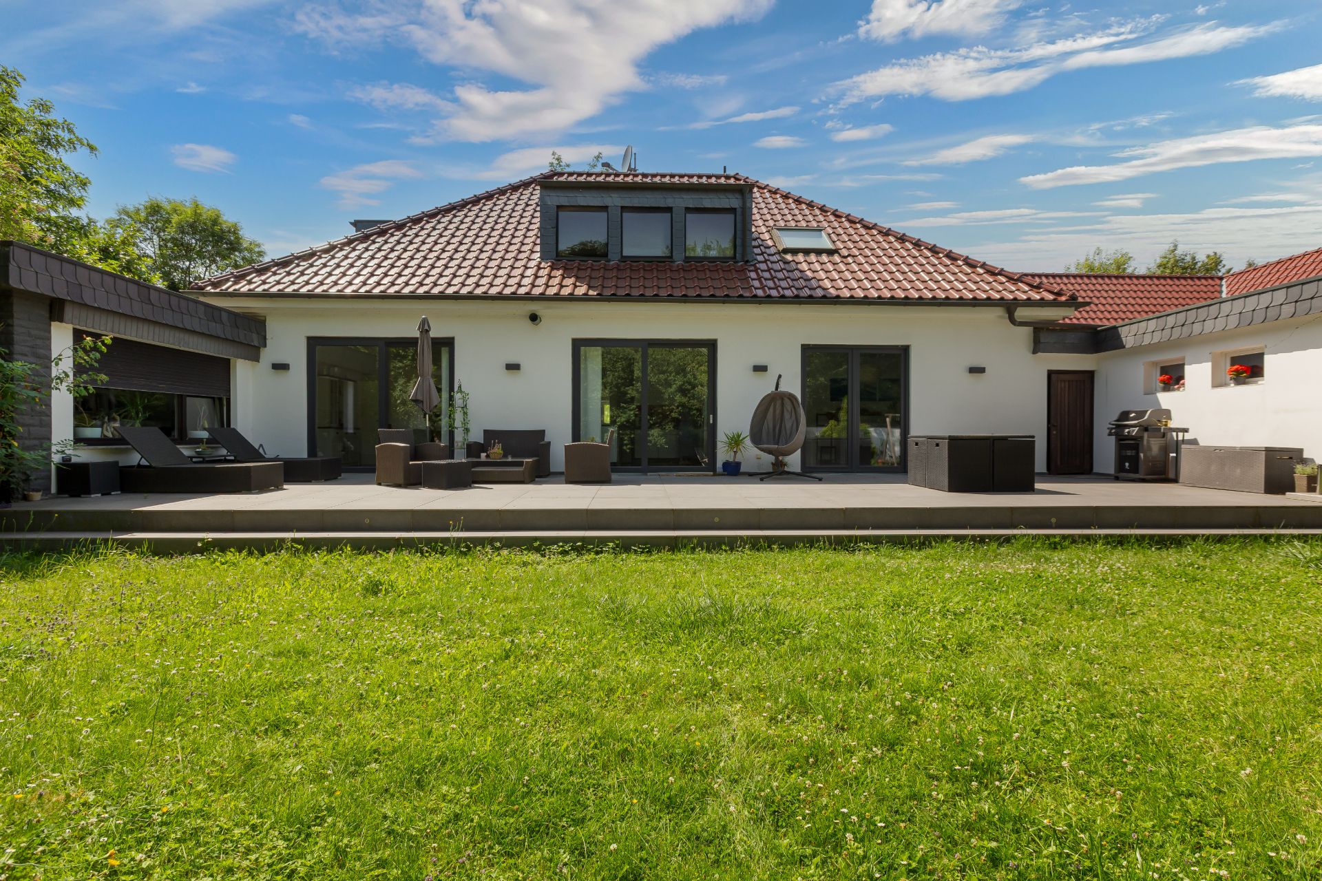 Modernes Einfamilienhaus mit großer Terrasse und Garten bei sonnigem Wetter.
