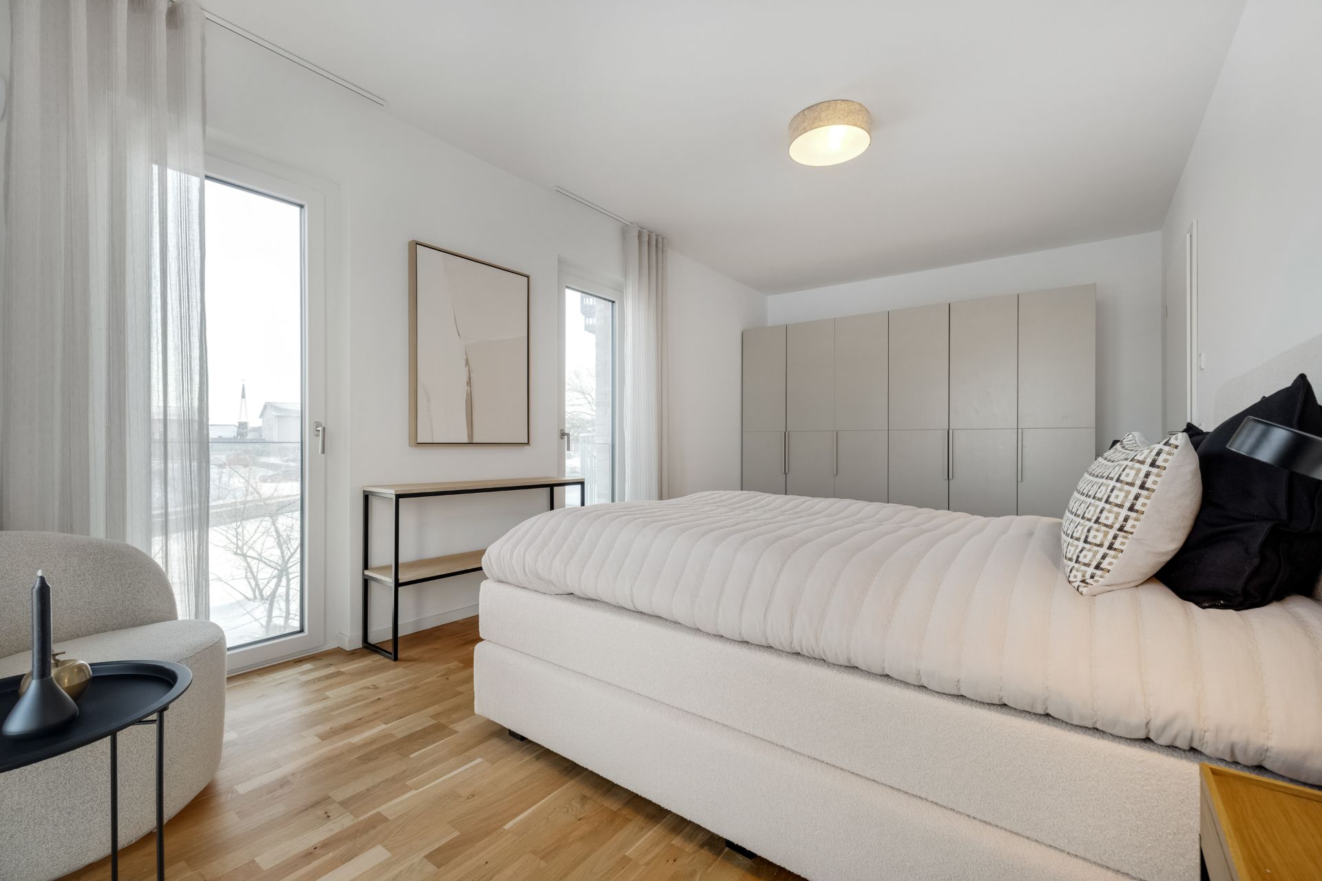 Helles Schlafzimmer mit großem Bett, Kleiderschrank und bodentiefen Fenstern.