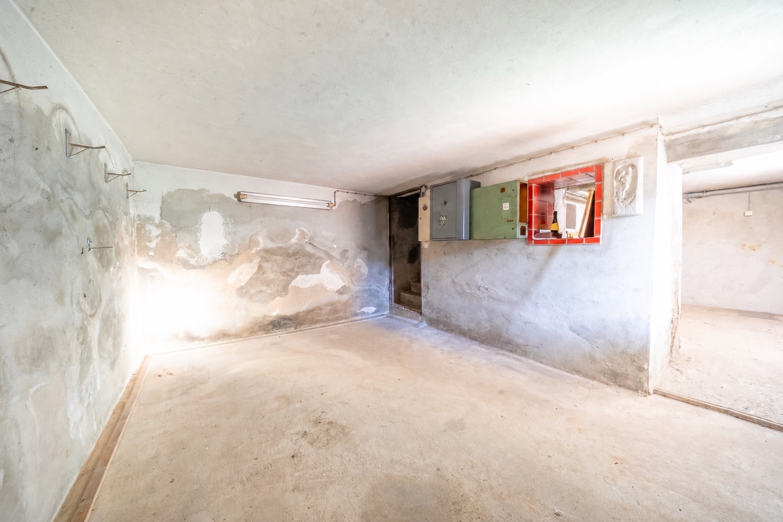 Heller, leerer Kellerraum mit Betonboden und sichtbaren Wandkästen.
