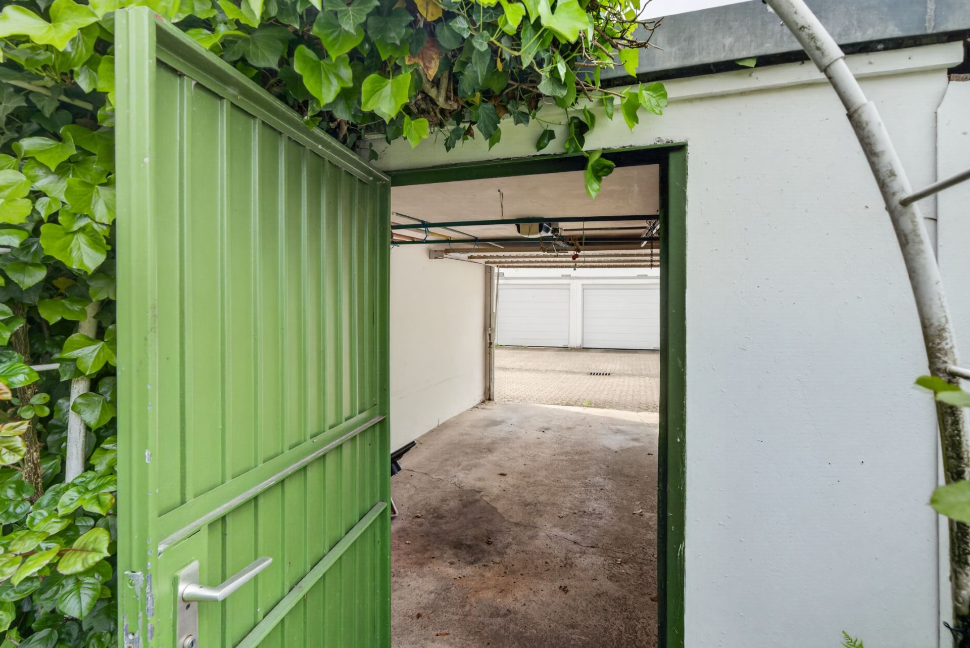 Offene grüne Tür führt in eine leere Garage mit Blick auf Garagentore draußen.