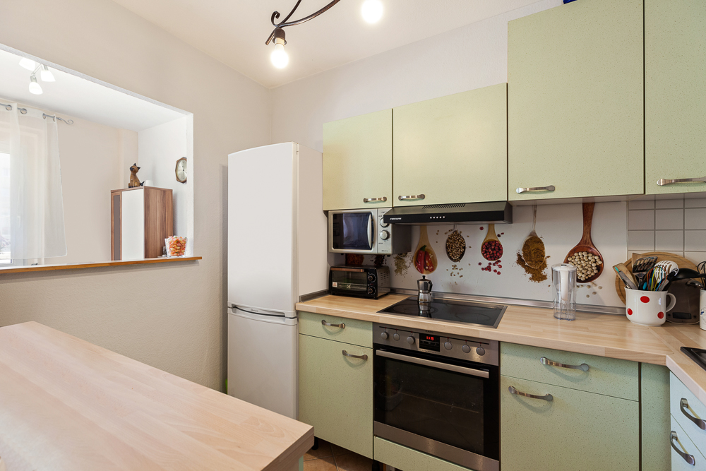 Helle Küche mit grünen Schränken, weißem Kühlschrank und dekorativen Löffeln an der Wand.