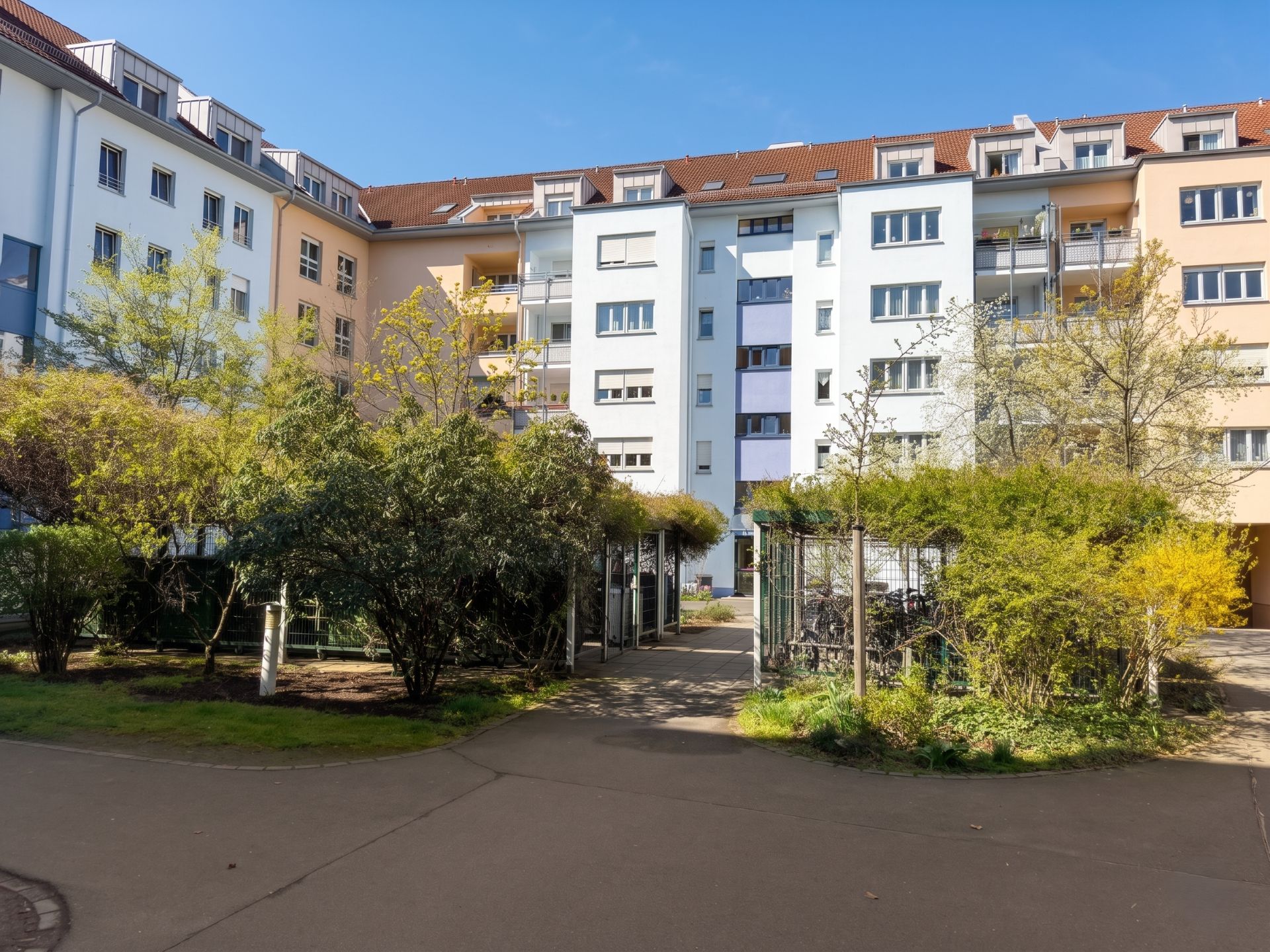 Mehrstöckiges Wohnhaus mit Balkonen und begrüntem Innenhof bei sonnigem Wetter.