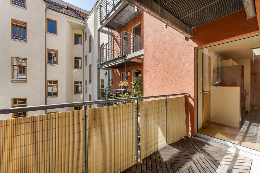 Balkon mit Holzboden und Bambusverkleidung, Blick auf benachbarte Wohnungen und Fenster.