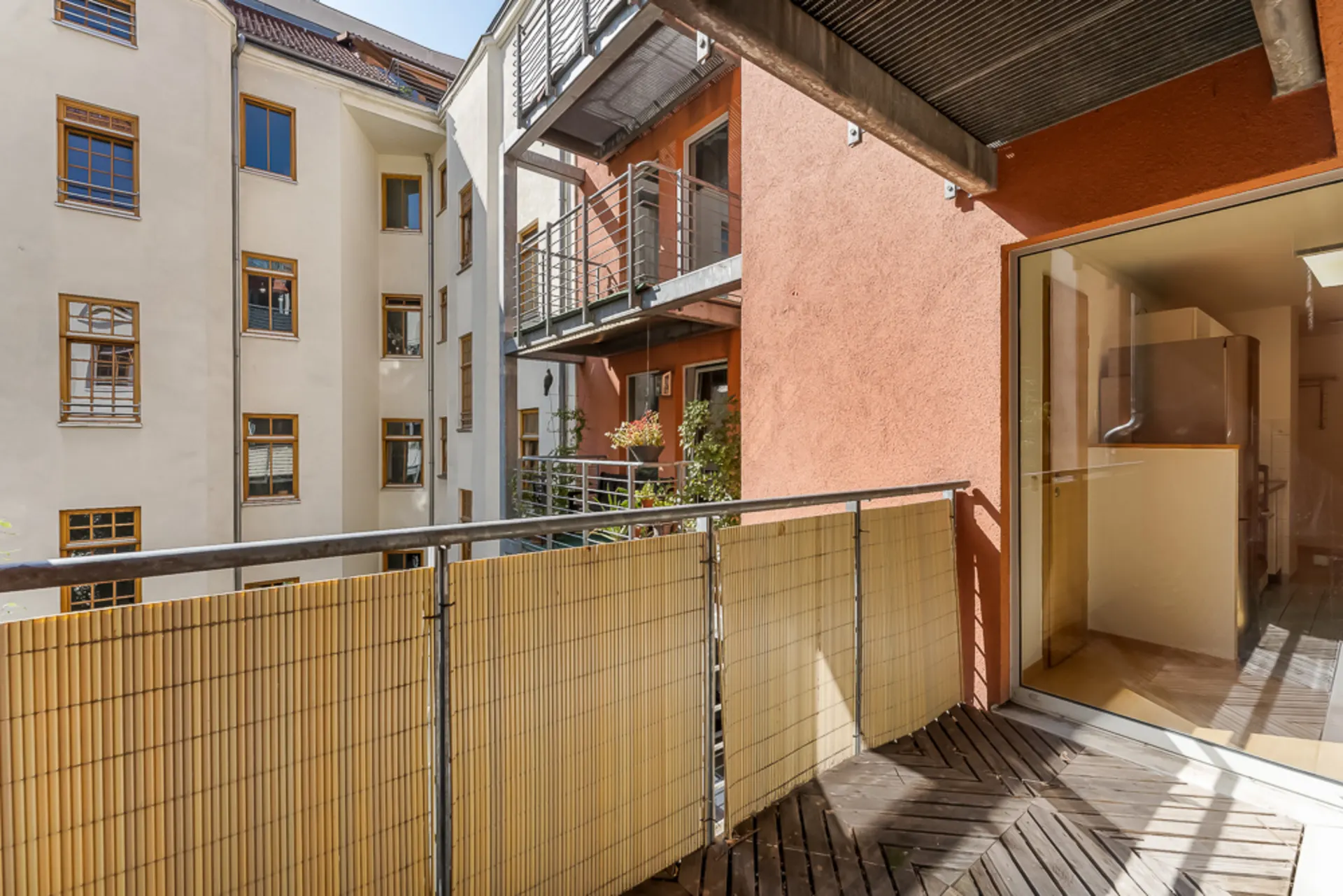 Balkon mit Holzboden und Bambusverkleidung, Blick auf benachbarte Wohnungen und Fenster.