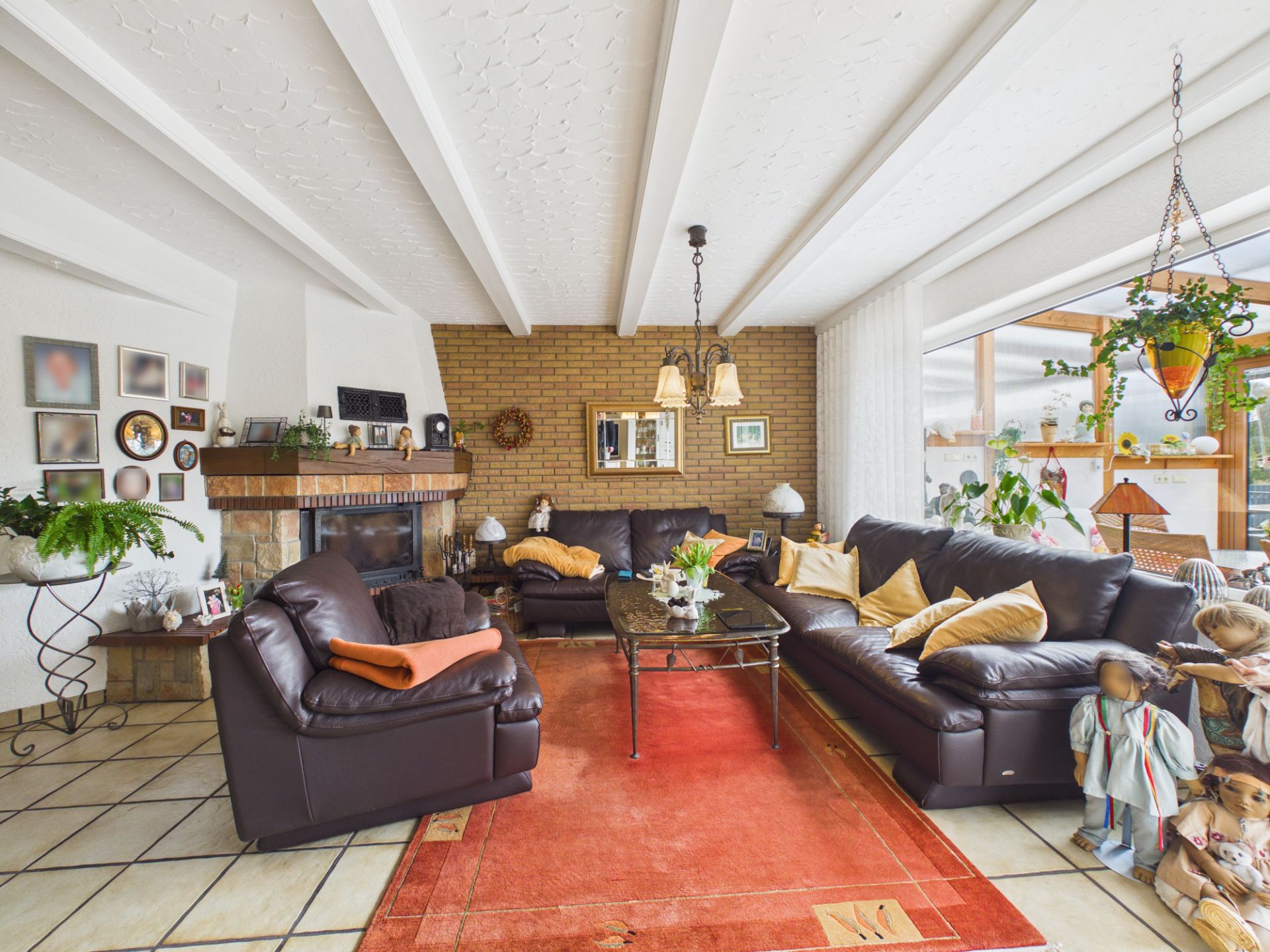 Wohnzimmer mit braunen Ledersofas, Kamin, rotem Teppich und vielen Pflanzen.