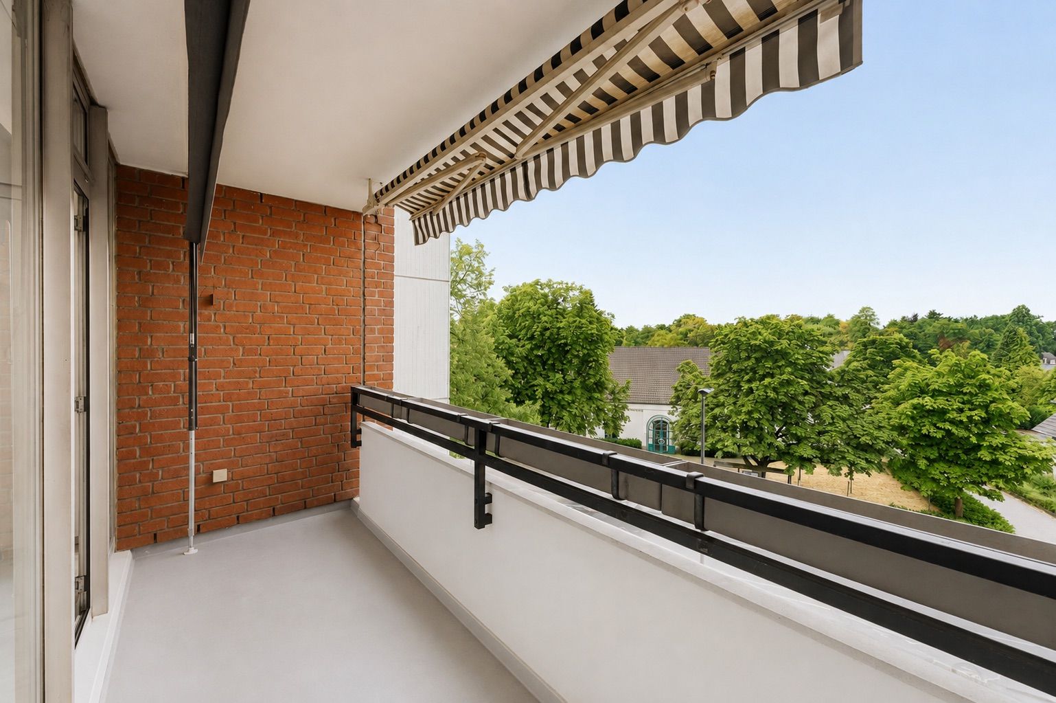 Balkon mit Markise, Blick auf grüne Bäume und Gebäude im Hintergrund.