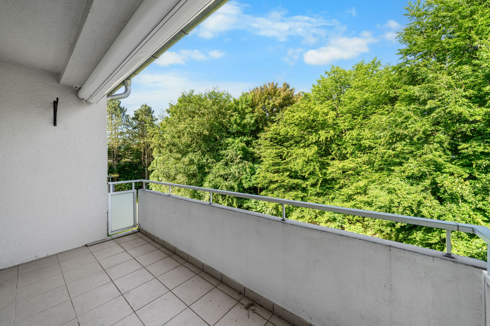 Großer Balkon mit Fliesenboden und Blick auf grüne Bäume.