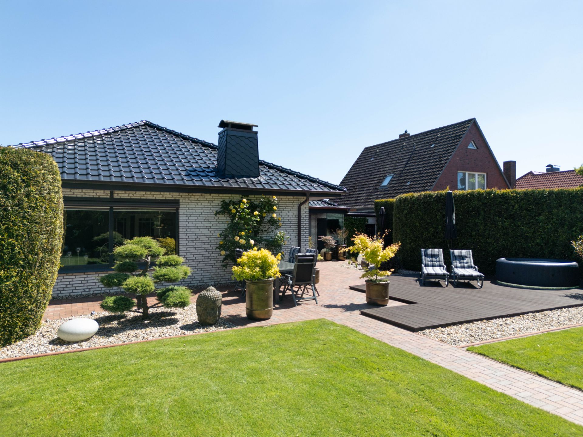 Gepflegter Garten mit Rasen, Terrasse, Liegestühlen und modernen Pflanzkübeln vor einem Einfamilienhaus.