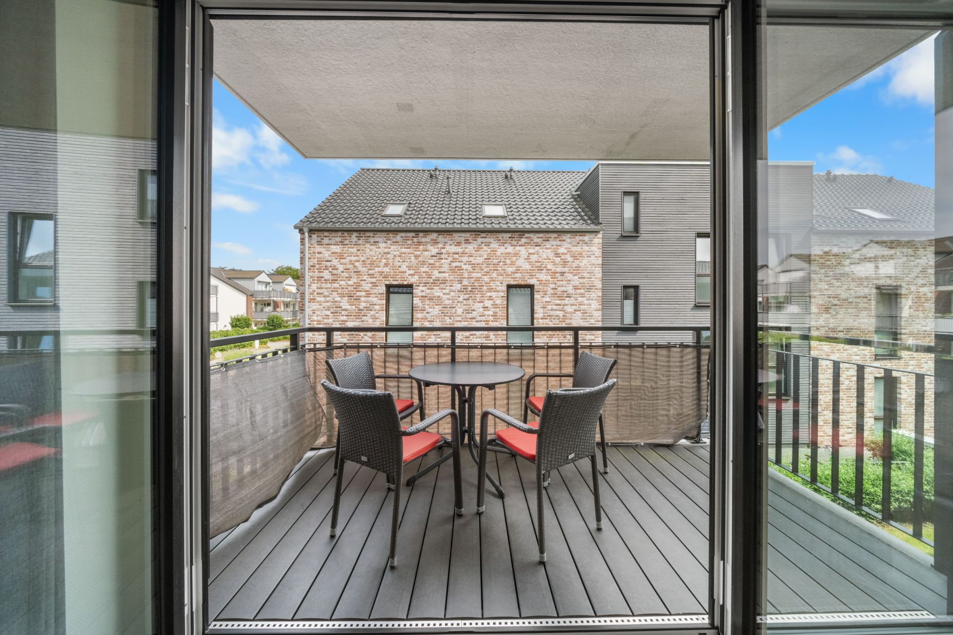Balkon mit rundem Tisch und vier Stühlen, Blick auf benachbarte Wohnhäuser.