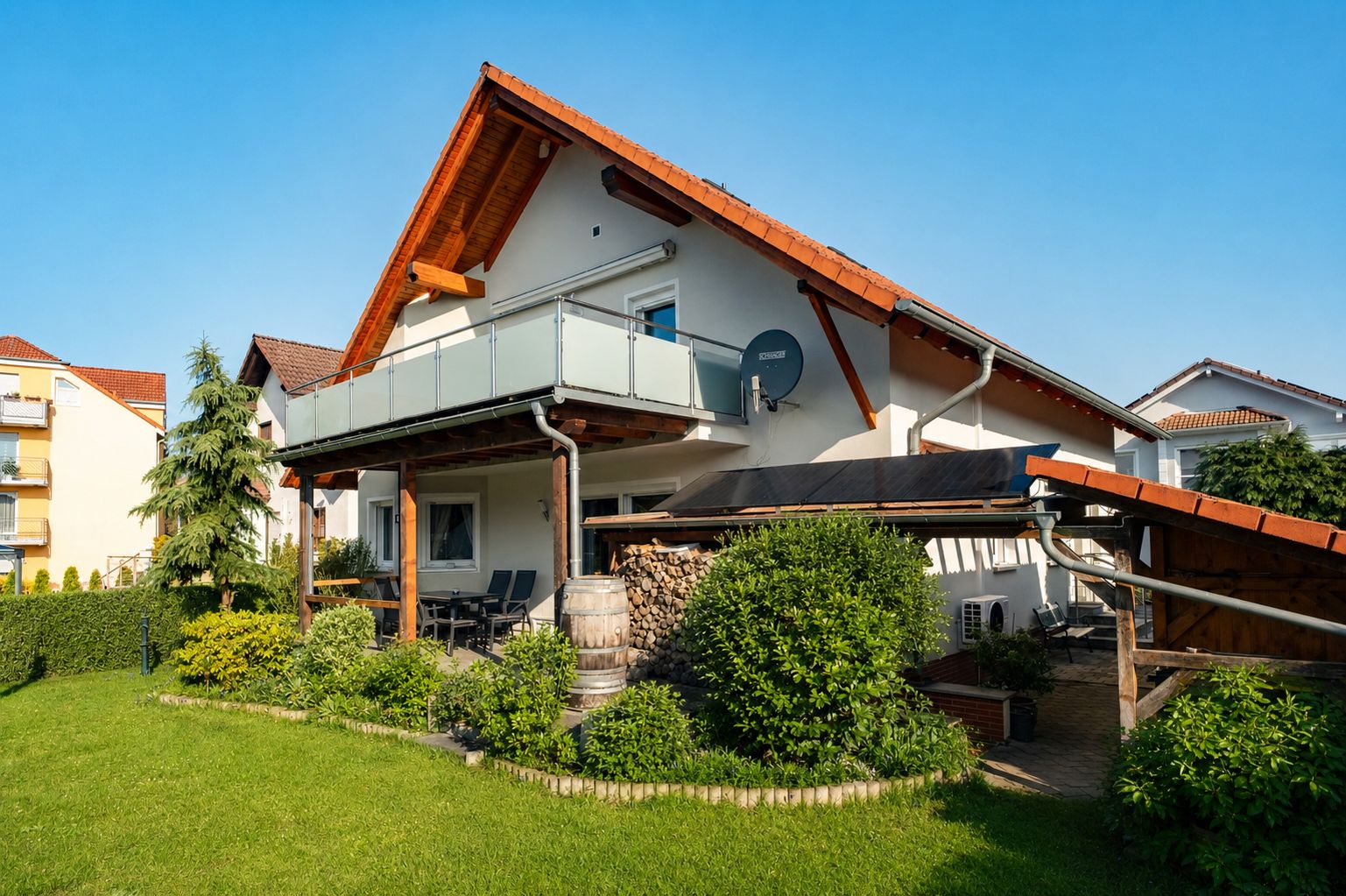Modernes Einfamilienhaus mit Balkon, Garten und überdachter Terrasse bei sonnigem Wetter.