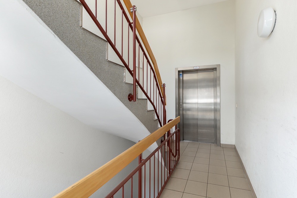 Treppenhaus mit rotem Geländer und Aufzugstür in einem Wohngebäude.