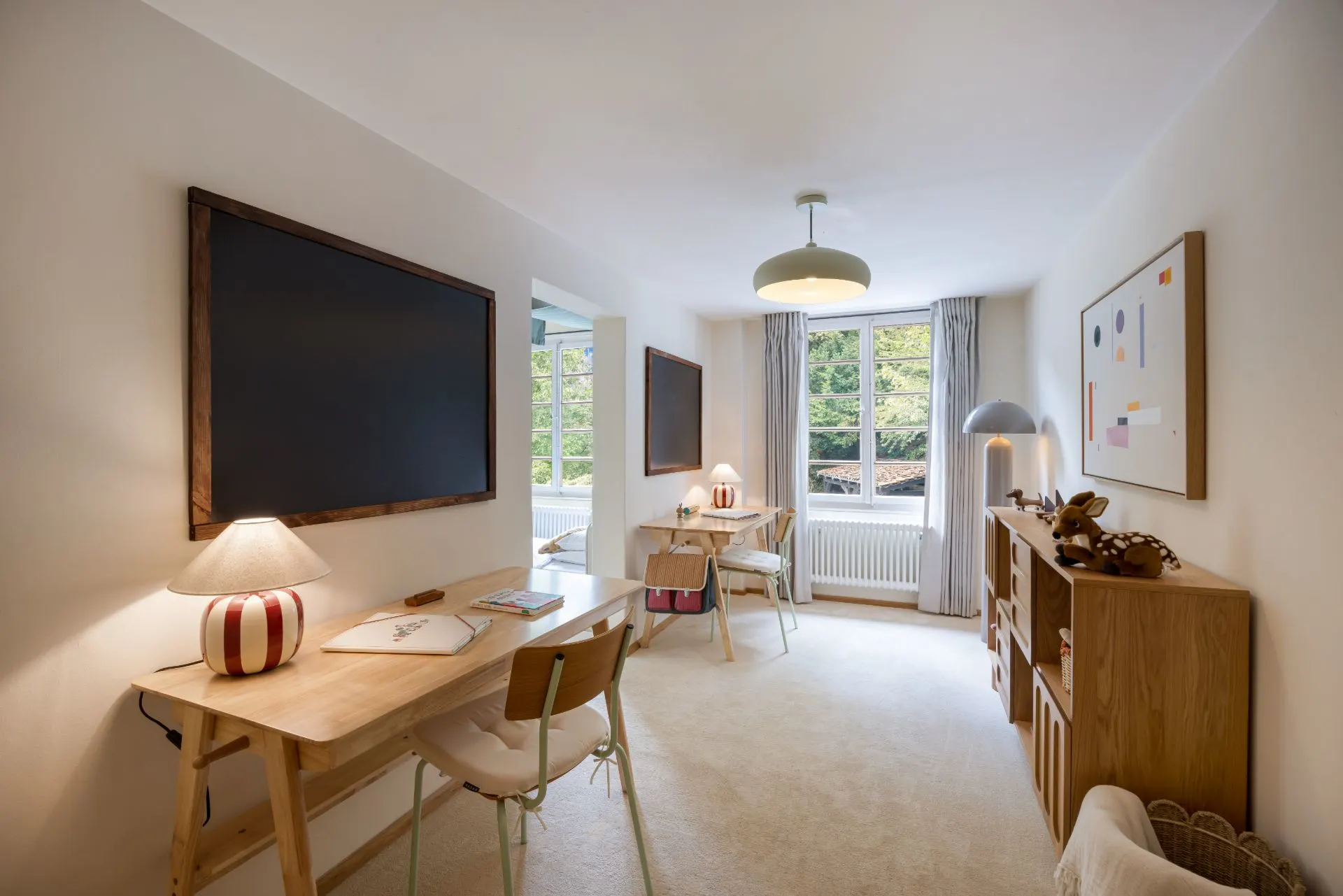Helles Arbeitszimmer mit zwei Schreibtischen, Regalen und großen Fenstern.