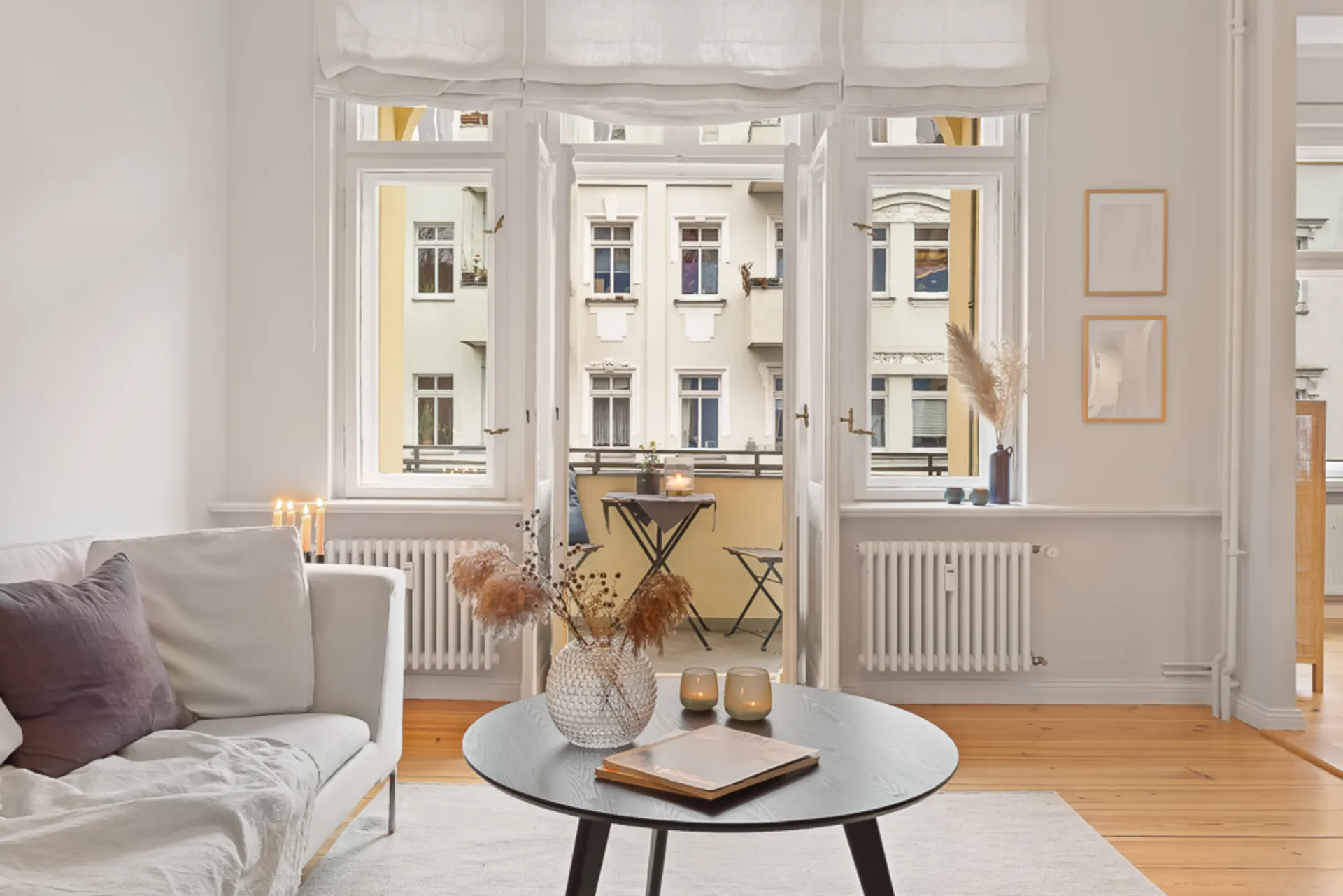 Helles Wohnzimmer mit Sofa, rundem Tisch und Blick auf einen kleinen Balkon mit Stühlen.