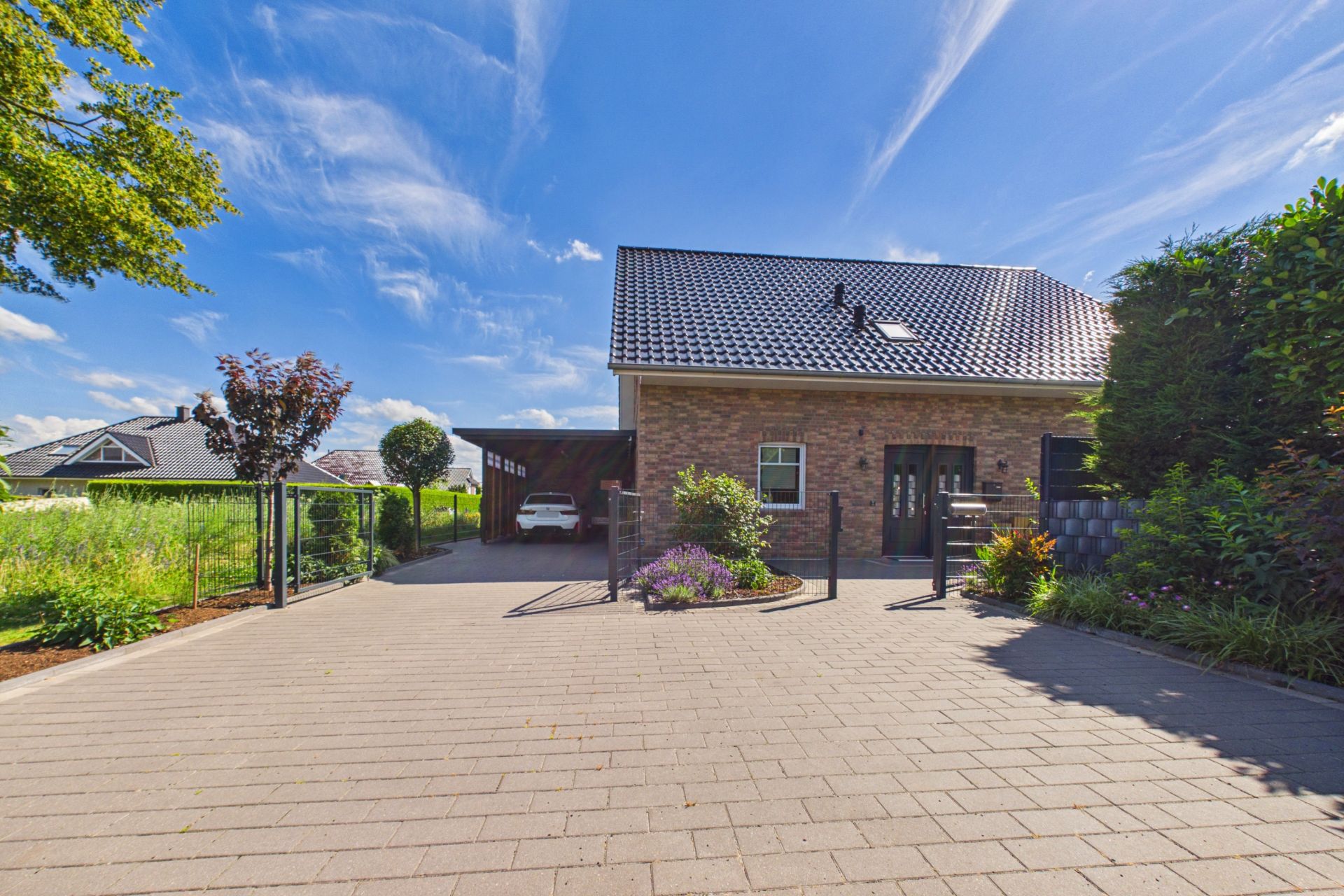Modernes Einfamilienhaus mit Ziegeldach, gepflasterter Einfahrt und Garten bei sonnigem Wetter.