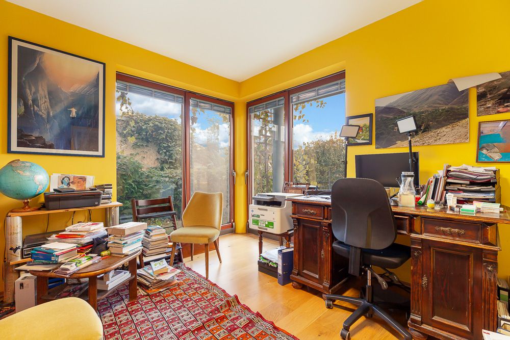 Helles Arbeitszimmer mit gelben Wänden, Schreibtisch, Bürostuhl, Computer und vielen Büchern.
