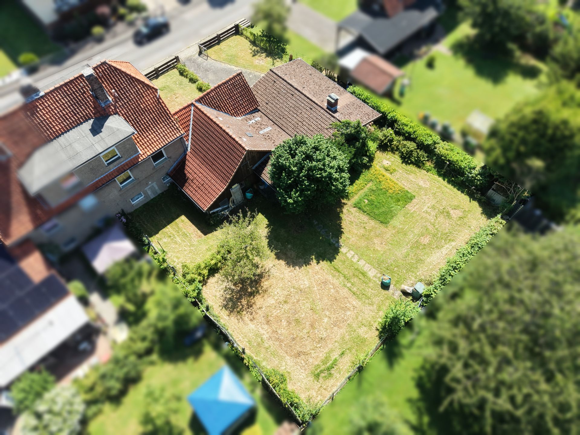 Luftbild eines Hauses mit rotem Dach und großem Garten, umgeben von Hecken.