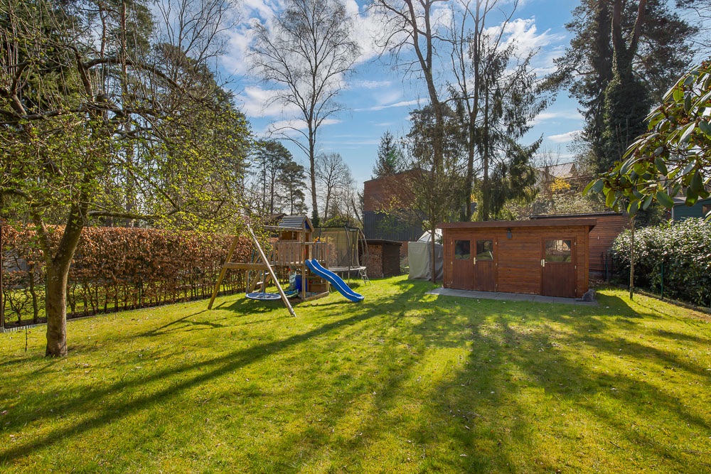Grüner Garten mit Spielplatz, Rutsche und Holzhaus im Hintergrund.
