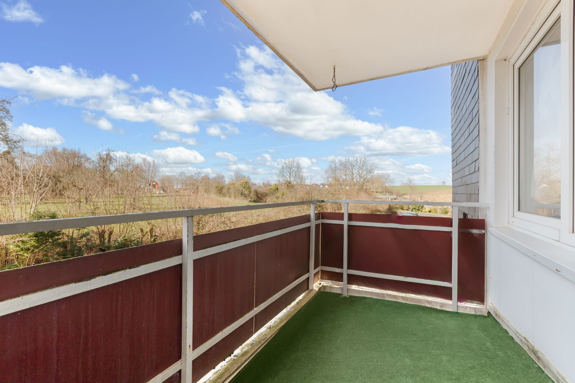 Balkon mit grünem Bodenbelag, Geländer und Blick auf eine Landschaft mit Bäumen.