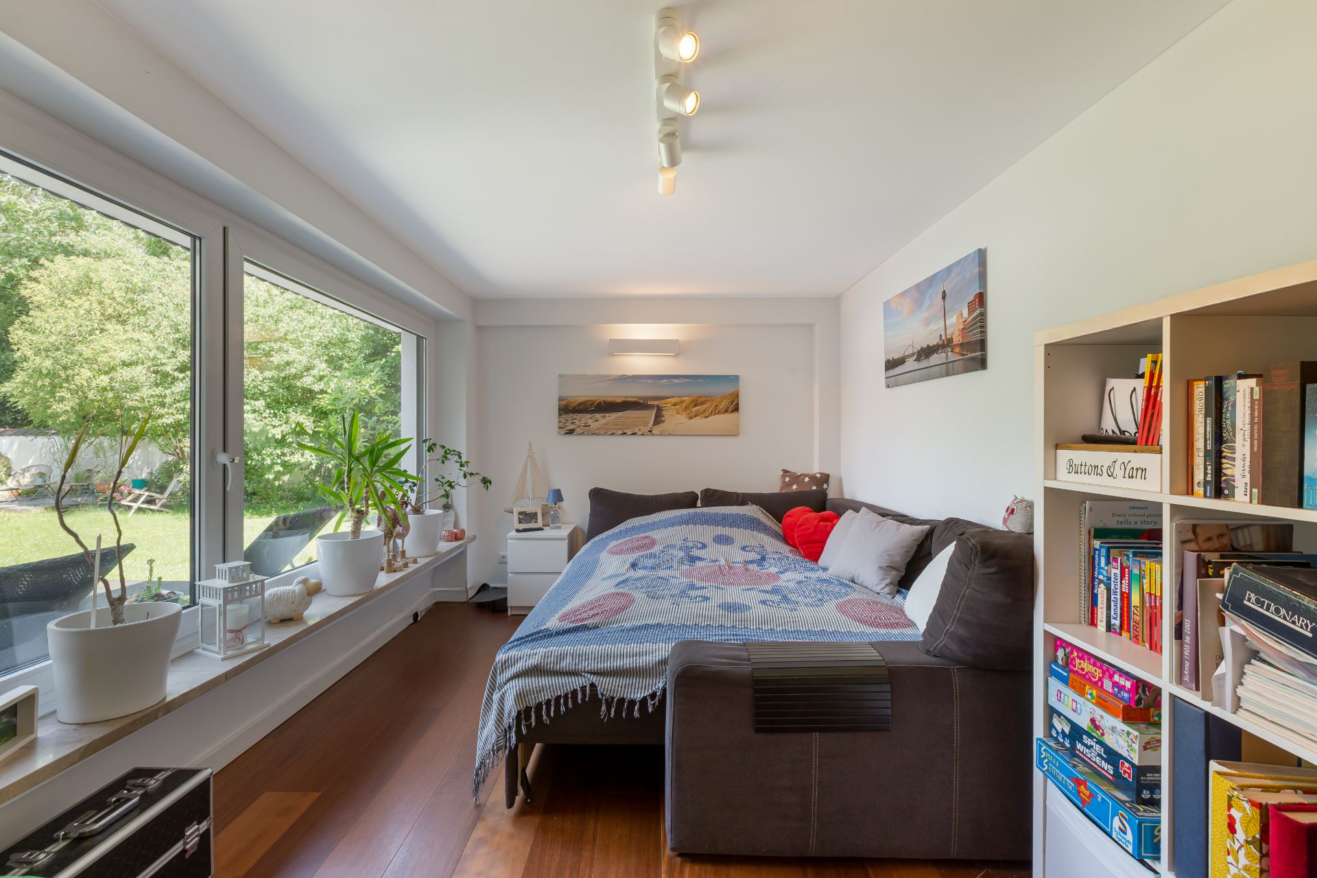 Helles Wohnzimmer mit Sofa, Bücherregal, großen Fenstern und Blick in den Garten.