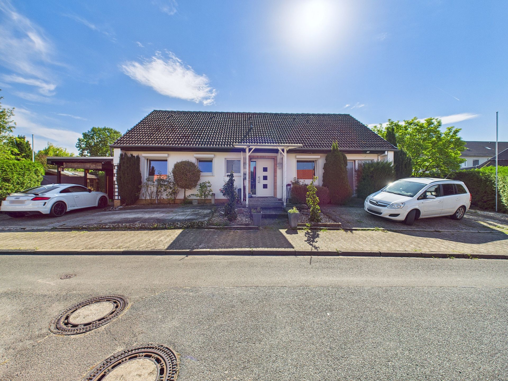 Einfamilienhaus mit dunklem Dach, Vorgarten und zwei geparkten Autos vor dem Haus.