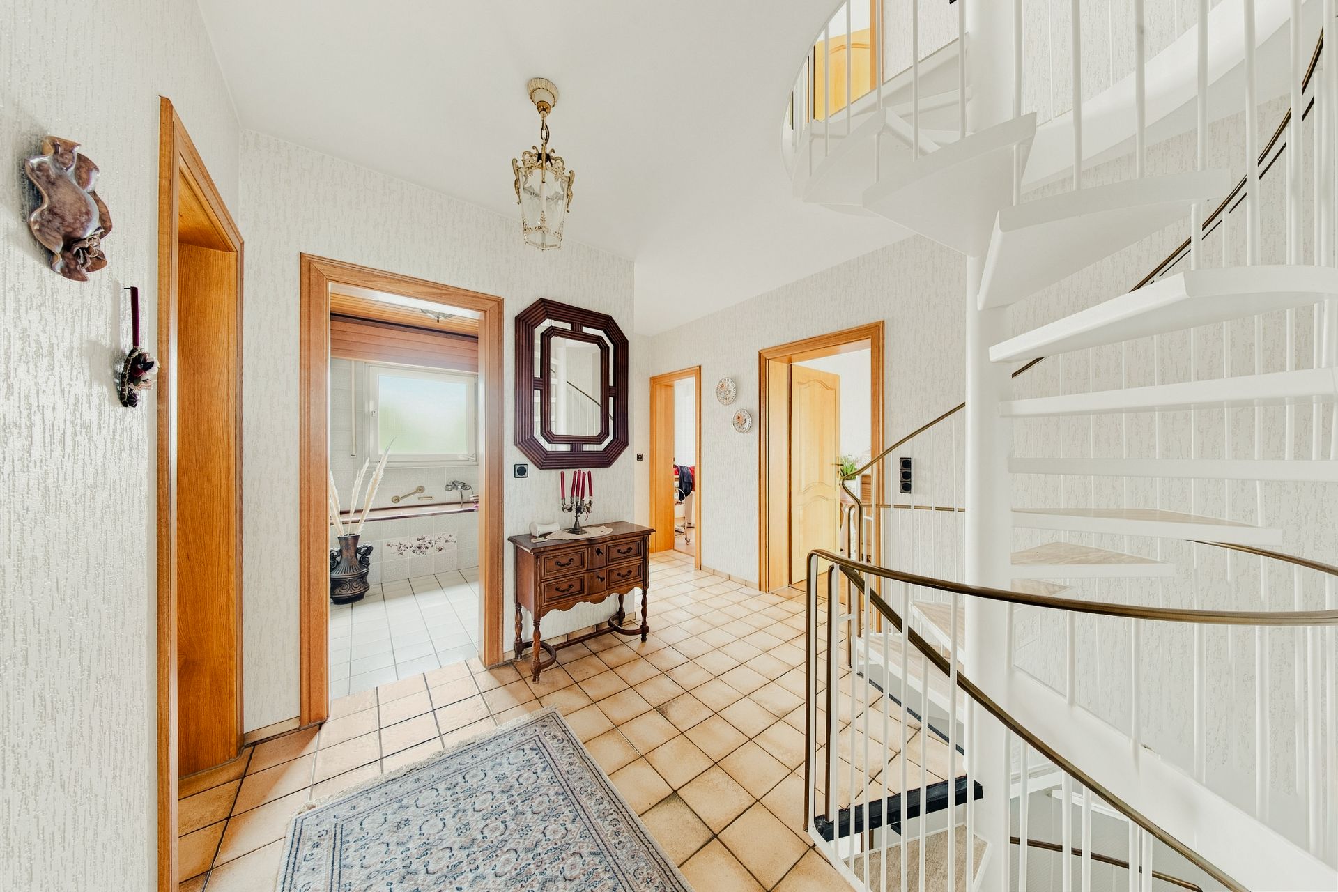 Heller Flur mit weißer Wendeltreppe, Spiegel, Teppich und mehreren Holztüren.