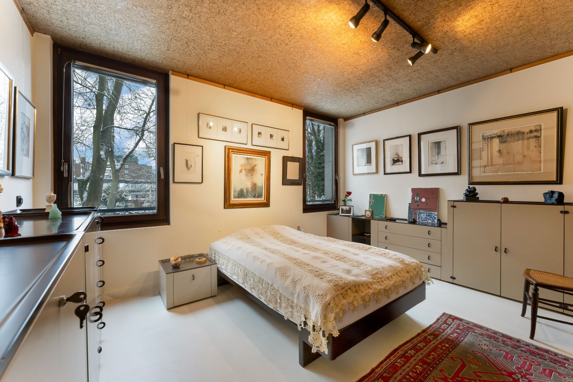 Schlafzimmer mit Doppelbett, großen Fenstern, Bildern an den Wänden und mehreren Kommoden.