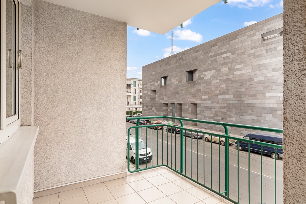 Balkon mit grünem Geländer und Blick auf eine Straße und ein modernes Gebäude.