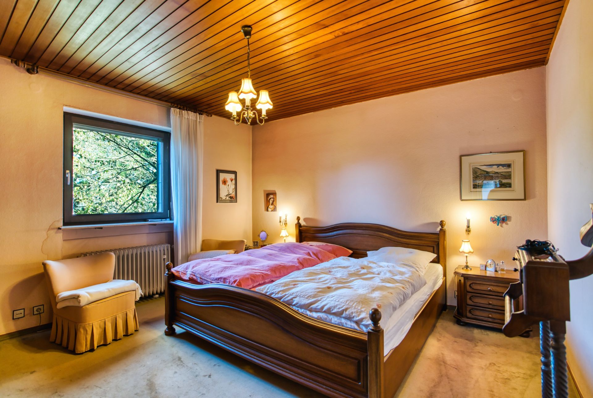 Gemütliches Schlafzimmer mit Doppelbett, Holzmöbeln, Sessel und Fenster mit Blick ins Grüne.