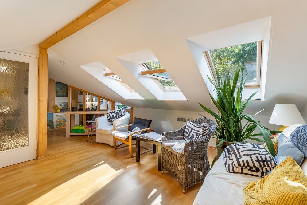 Helles Wohnzimmer mit Dachfenstern, Holzboden, Pflanzen und gemütlichen Sitzmöbeln.