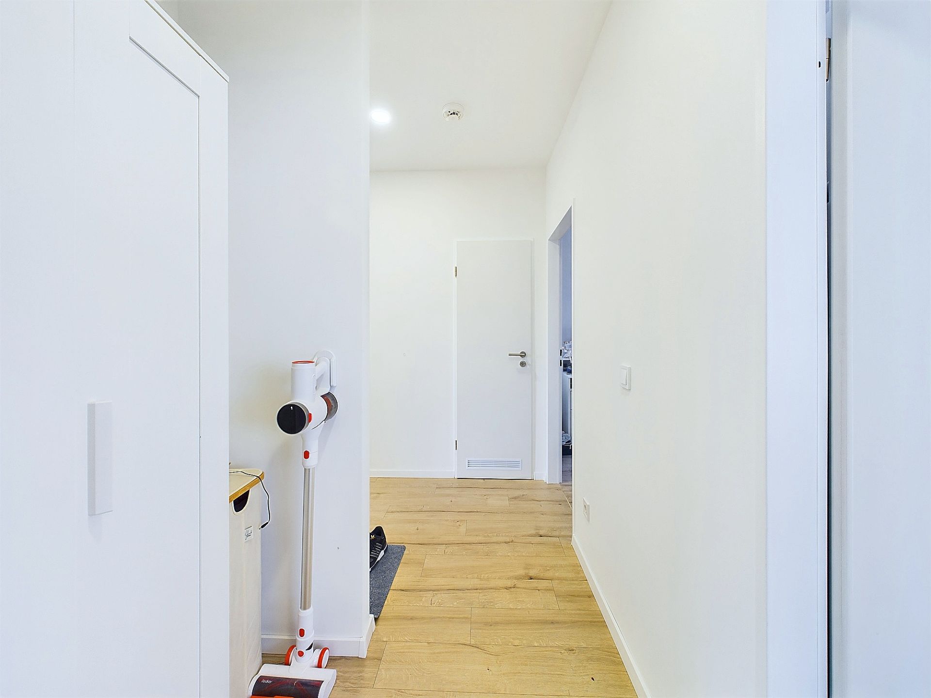 Heller Flur mit Holzboden, weißem Schrank und kabellosem Staubsauger an der Wand.