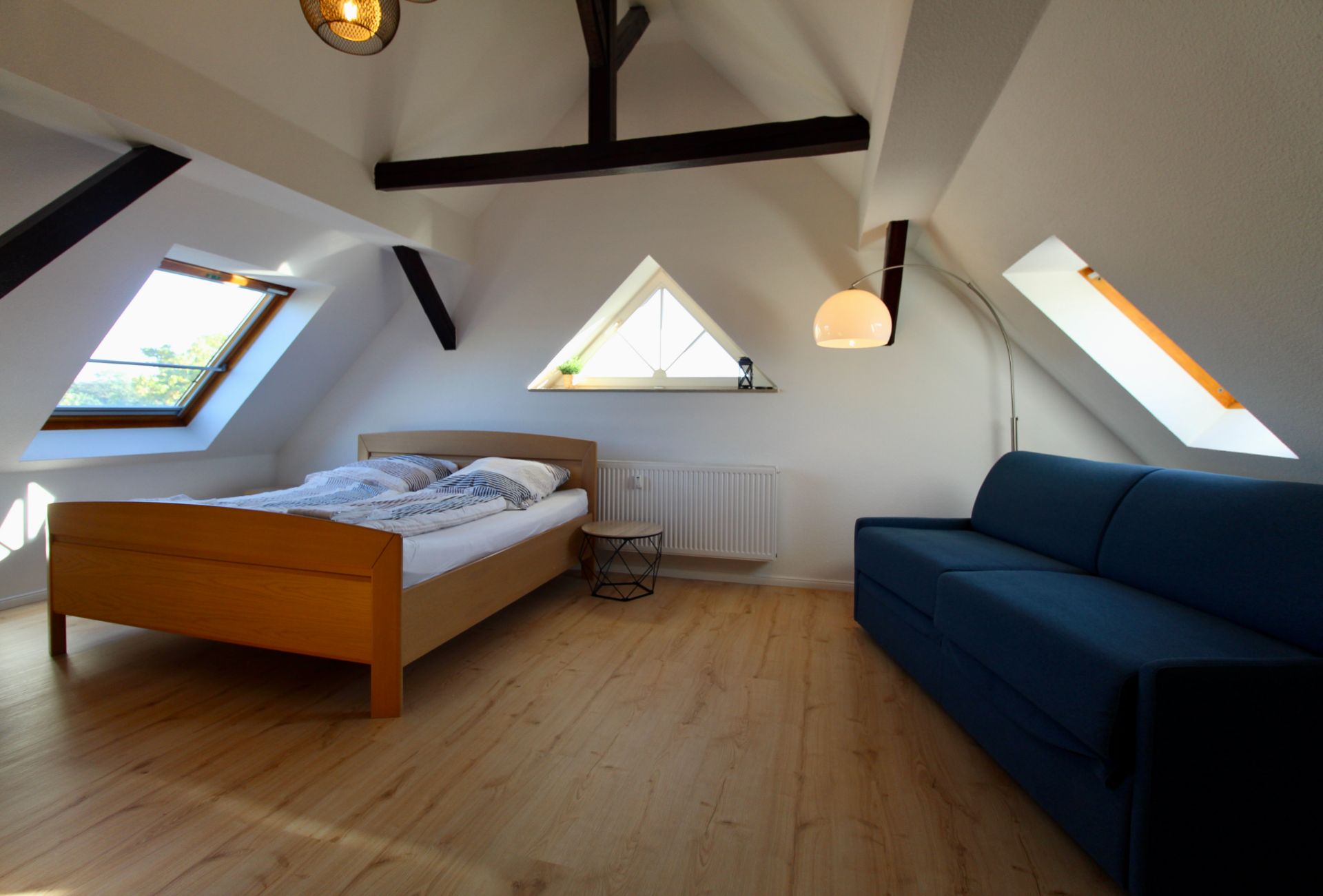 Helles Schlafzimmer mit Holzbett, blauer Couch und Dachfenstern in einem Dachgeschoss.