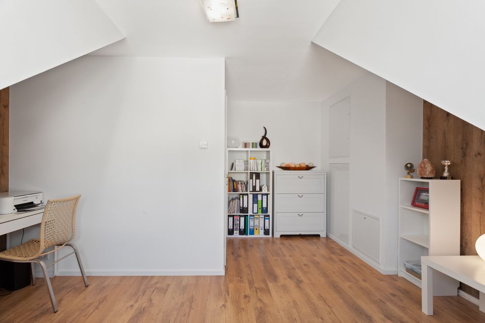 Heller Raum mit Schreibtisch, Regal, Kommode und Bücherregalen auf Holzfußboden.