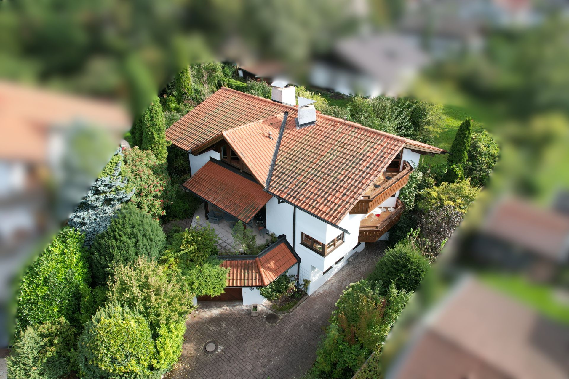 Großes weißes Haus mit rotem Ziegeldach, Balkon und umgeben von grünem Garten.