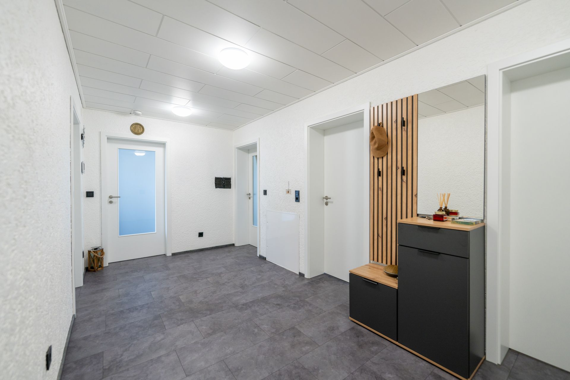 Heller Flur mit grauem Boden, vier Türen und einer Garderobe mit Spiegel und Hut.