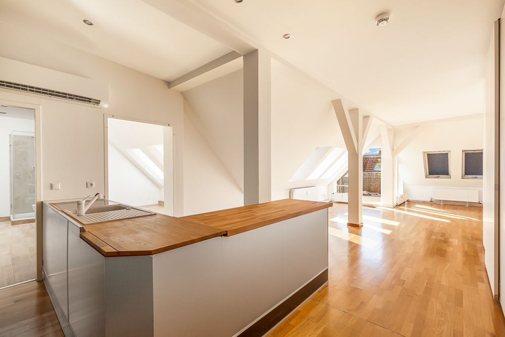 Helle Dachgeschosswohnung mit offener Küche, Holzfußboden und großen Fenstern.