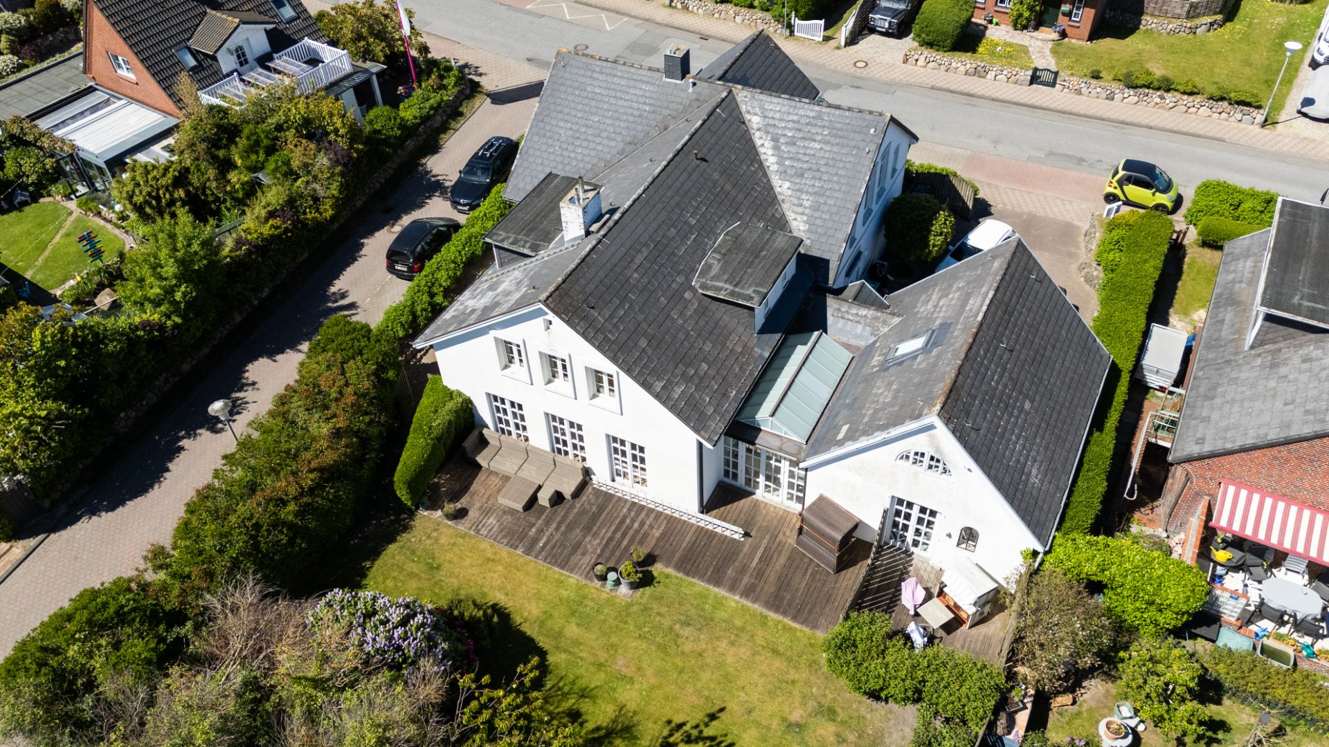 Luftaufnahme eines weißen Wohnhauses mit großem Holzbalkon und Garten.