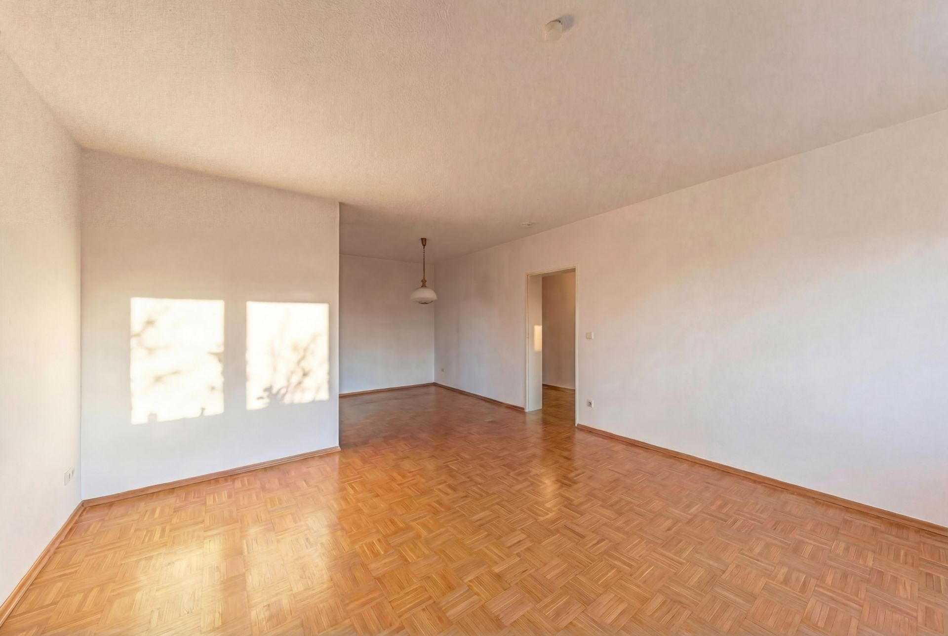 Leerer Raum mit Parkettboden, weißen Wänden und einer Deckenlampe.