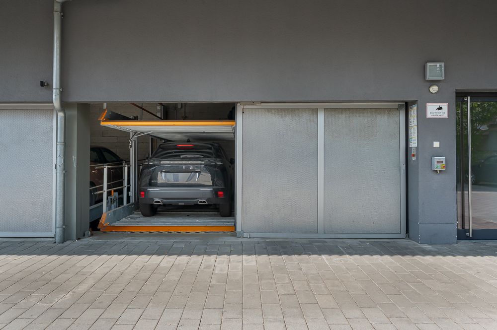 Zwei Autos parken gestapelt in einer automatischen Garage mit grauen Wänden.