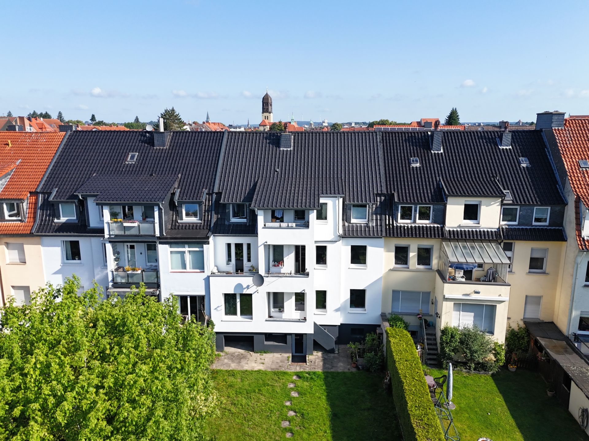 Mehrfamilienhaus mit Balkonen, dunklem Dach und Garten im Vordergrund, aufgenommen bei Tageslicht.