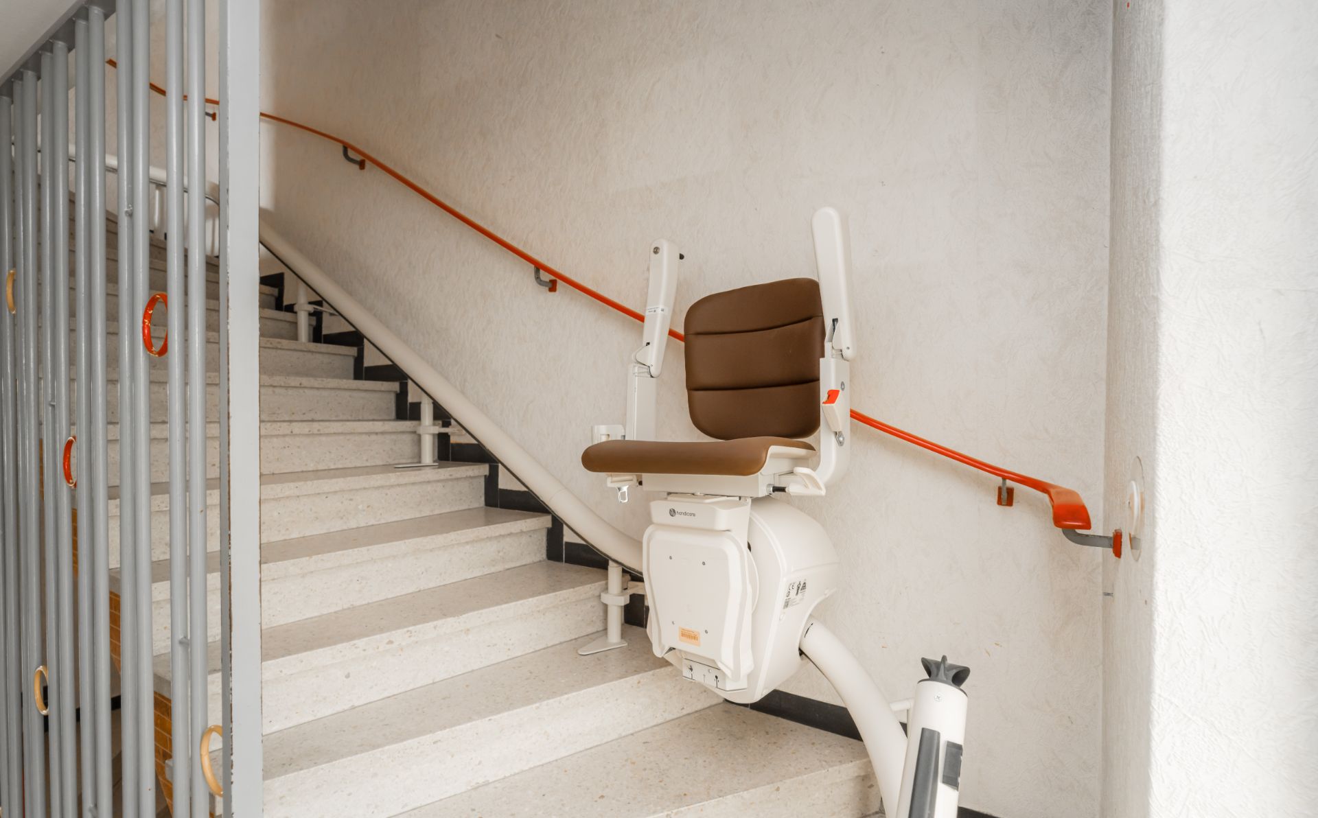 Treppenlift auf einer Innentreppe mit braunem Sitz und orangem Handlauf.